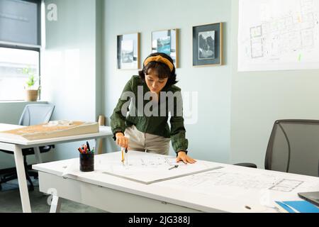 Jeune architecte asiatique dessinant un plan à table dans un bureau de création Banque D'Images