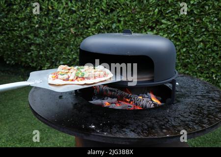 une pizza faite maison en train d'être pris d'un four à pizza extérieur au feu de bois Banque D'Images