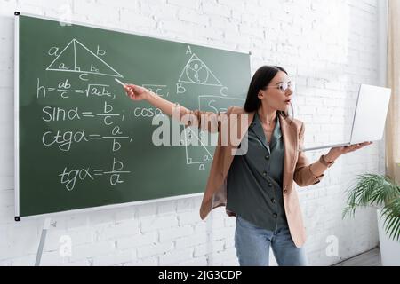 Professeur pointant vers des formules mathématiques sur le tableau de surveillance pendant la leçon en ligne en classe Banque D'Images