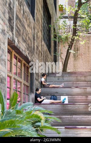 Un groupe de travailleurs indépendants travaillent sur un ordinateur portable à distance ou étudient dans un espace de travail extérieur situé sur un sol en bois Banque D'Images