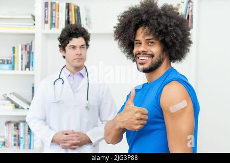 Homme afro-américain qui se montre sous le pouce après la vaccination contre Covid 19 comme protection contre le coronavirus Banque D'Images