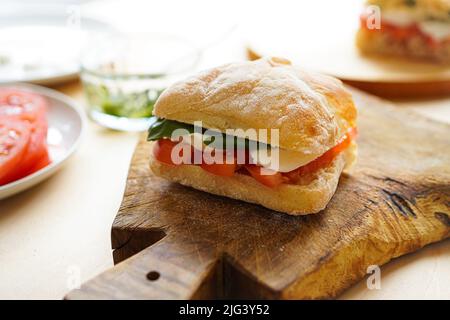 Préparation des PANINI italiens avec tomates et basilic à la table Banque D'Images