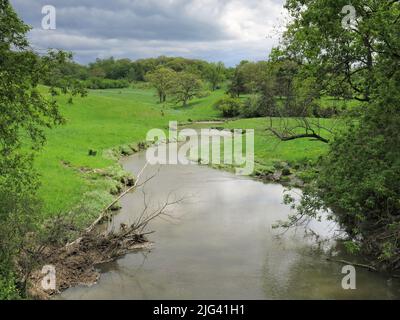 Un ruisseau tranquille serpente à travers des forêts luxuriantes et des pâturages tandis que les nuages de tempête se rassemblent au loin Banque D'Images