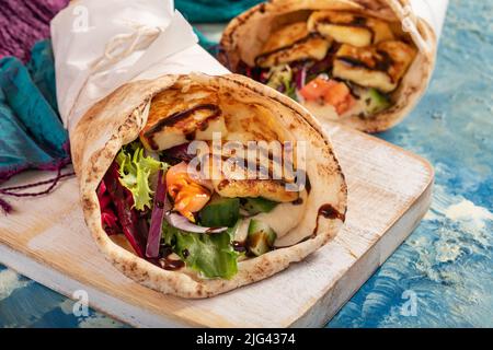 L'halloumi, le houmous et les légumes traditionnels méditerranéens grillés sont des roulés de pain plat recouverts d'herbes et de vinaigre balsamique sur fond bleu Banque D'Images