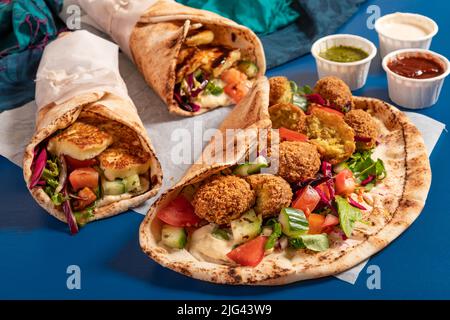 Traditionnel méditerranéen arabe halloumi et falafel grillé, houmous et légumes dans des roulés de pain plat avec des herbes et une variété de sauces Banque D'Images