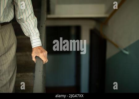 Le vieil homme se penche sur la main courante. Le vieil homme descend les escaliers. Détails de l'entrée. Intérieur de la maison. Banque D'Images