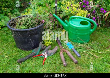 Jardin anglais de campagne début juillet. Une sélection d'outils bien utilisés à côté de la bordure mixte. Banque D'Images