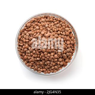 Vue de dessus des lentilles brunes sèches dans un bol en verre isolé sur du blanc Banque D'Images