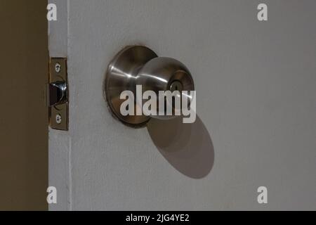 Vue rapprochée d'un bouton de porte rond en acier inoxydable sur une porte en bois blanc. Porte ouverte. Banque D'Images