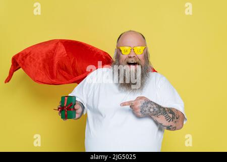 homme de taille plus stupéfié dans des lunettes avec le lettrage de vente et le cloak rouge pointant à présent isolé sur jaune Banque D'Images