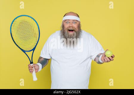 homme de grande taille avec balle de tennis et raquette regardant la caméra isolée sur jaune Banque D'Images