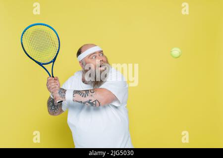 homme excités de plus grande taille avec tatouages jouant au tennis isolé sur jaune Banque D'Images