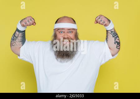 sportif tatoué en surpoids démontrant une force isolée sur le jaune Banque D'Images