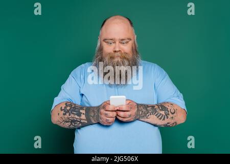 homme de taille plus excitée avec la barbe bavardant sur le smartphone isolé sur le vert Banque D'Images