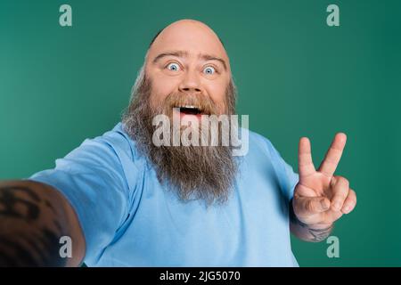 homme de grande taille stupéfié avec une barbe montrant un geste de victoire isolé sur le vert Banque D'Images