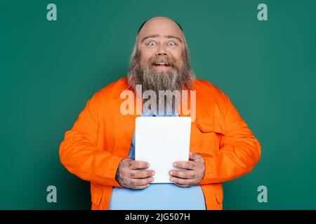 homme de grande taille, émerveillé et heureux, avec une barbe qui tient la tablette numérique isolée sur le vert Banque D'Images