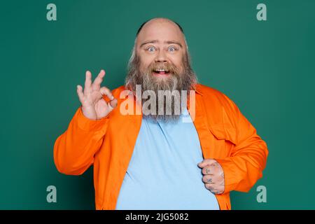 homme de grande taille excité en chemise orange montrant le signe ok isolé sur le vert Banque D'Images