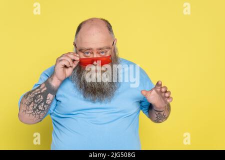 homme sérieux et de taille plus regardant l'appareil photo sur des lunettes de soleil tendance isolées sur jaune Banque D'Images