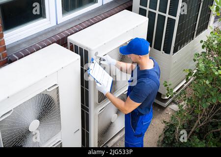 Deux électriciens hommes portant des vestes de sécurité Contrôle de l'unité de climatisation sur le toit du bâtiment Banque D'Images