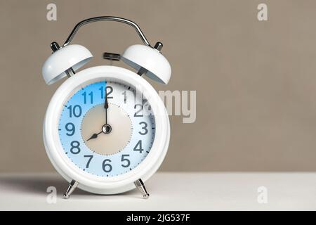 Huit heures sur l'alarme. Un réveil blanc se trouve sur une table blanche. La main de l'horloge pointe à 8 heures. Il est temps de passer à l'heure d'été ou d'hiver. Définir Banque D'Images