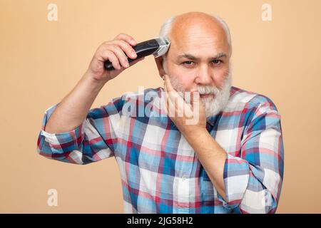 Portrait d'un homme âgé en train d'être tondu avec une tondeuse électrique professionnelle dans un salon de coiffure, coupe de cheveux avec un rasoir électrique. Banque D'Images