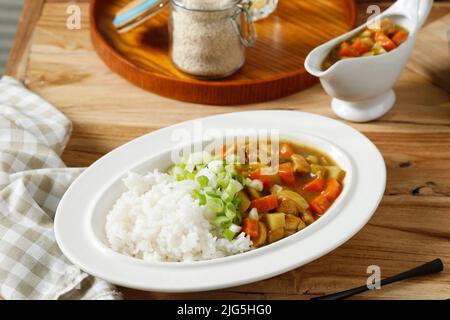 Riz au curry japonais avec viande, carotte et pomme de terre avec oignon vert haché sur le dessus. Gros plan sur la plaque blanche sur la table en bois. Banque D'Images