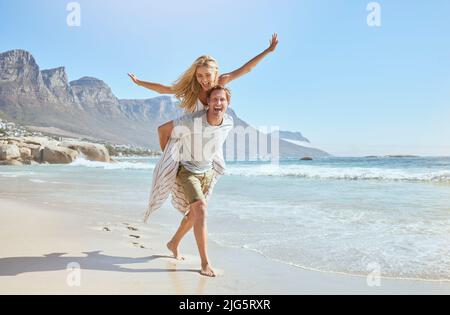 Portrait d'un jeune couple heureux et aimant appréciant une journée à la plage en été. Gai affectueux mari donnant à sa femme joyeuse un cogempyback pendant Banque D'Images