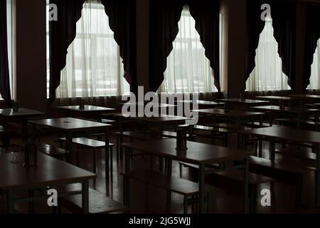 Rideaux dans la salle à manger. Beaucoup de tables. Lumière des grandes fenêtres. Les bureaux se tiennent en rangée. Banque D'Images