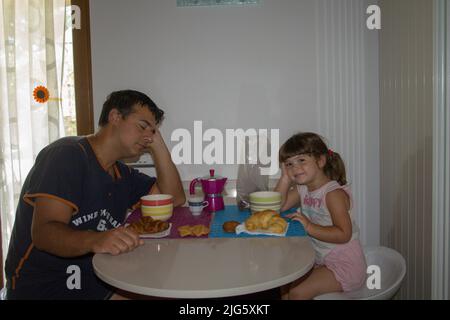 Photo d'un papa endormi et juste réveillant avec sa fille tout en prenant le petit déjeuner le matin. Banque D'Images