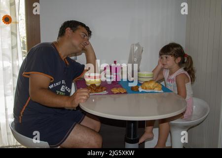 Photo d'un papa endormi et juste réveillant avec sa fille tout en prenant le petit déjeuner le matin. Banque D'Images