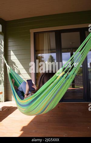 Femme se détendant dans un hamac près de la maison pendant une journée d'été et utilise un smartphone Banque D'Images