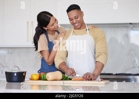 Un jeune couple latin aimant cuisant un dîner sain ensemble à la maison. Un homme aimant coupant des carottes et d'autres aliments de légumes, préparant un repas et Banque D'Images