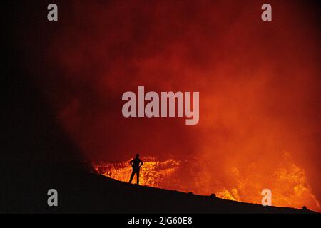 Un explorateur pose près du bord du cratère alors qu'il regarde dans l'évent de Murum, sur l'île d'Ambrym à Vanuatu, au cours d'une expédition pour cartographier le cratère. Banque D'Images