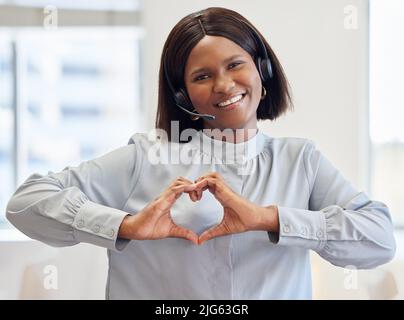 J'aime pouvoir aider les gens. Photo d'un agent de service à la clientèle attrayant debout seul au bureau et montrant un geste de main en forme de cœur. Banque D'Images