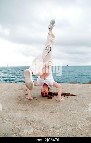 Danseuse de breakdance faisant une stand à la main à l'extérieur près de la mer. Banque D'Images