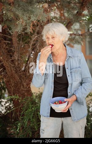 Femme âgée tenant un bol de fraises mûres Banque D'Images