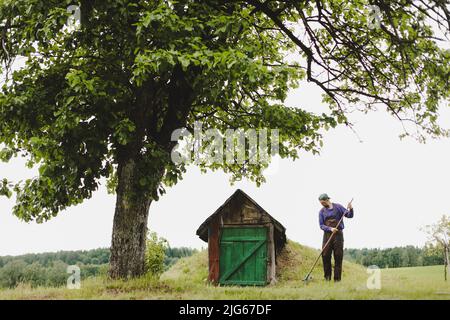 Homme travaillant dans le jardin avec râteau dans une journée ensoleillée. Agriculteur travaillant dans l'arrière-cour Banque D'Images