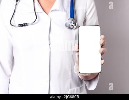 Médecin tenant un téléphone avec écran de maquette. Médecine en ligne, utilisant l'application médicale dans le concept de smartphone, de télésanté, de télémédecine. Femme en blouse de laboratoire avec stéthoscope et gants. Photo de haute qualité Banque D'Images