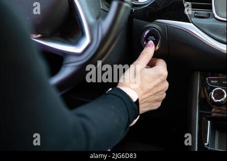 La femme démarre le moteur de la voiture avec le bouton START-STOP. Intérieur de voiture moderne, gros plan Banque D'Images