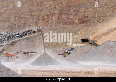 Un convoyeur qui déverse du gravier alors qu'un chargeur frontal déverse du gravier dans une trémie pour le criblage d'une mine de gravier industrielle dans l'Utah. Banque D'Images