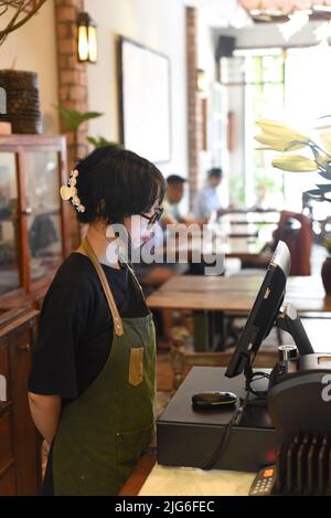 Jeune serveuse vietnamienne servant un client à la caisse dans le café. Banque D'Images