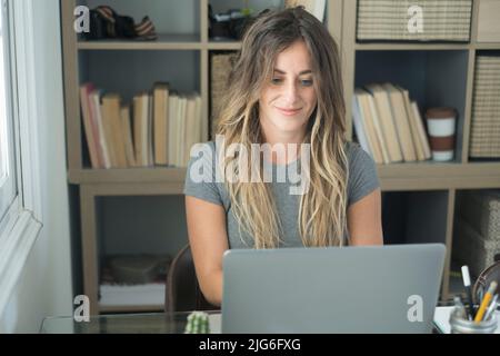 La jeune femme moderne du millénaire travaille sur un ordinateur au bureau dans un autre poste de travail professionnel de bureau à domicile. Une femme sourit et regarde l'écran d'un pc. Freelan Banque D'Images