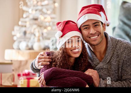 Je suis si heureux de passer Noël avec vous. Photo d'un jeune couple portant des chapeaux de Noël assis à la maison. Banque D'Images