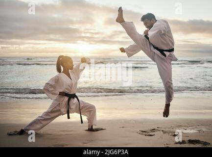 Karaté toute la journée. Photo de deux jeunes artistes martiaux pratiquant le karaté sur la plage. Banque D'Images
