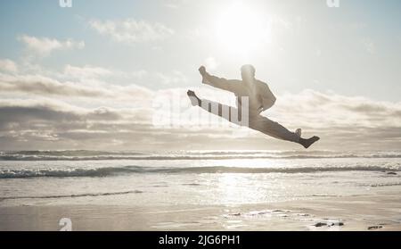 Puissance et précision. Photo en longueur d'un beau jeune homme d'art martial pratiquant le karaté sur la plage. Banque D'Images