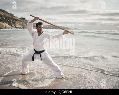 Bojustiu. Photo en longueur d'un beau jeune homme d'art martial pratiquant le karaté sur la plage. Banque D'Images