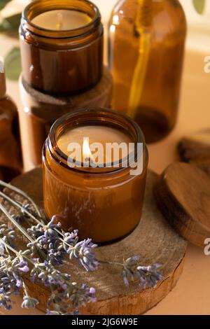 Bougies de soja dans un pot en verre. Aromathérapie. Bougie brûlante et lavande. Couvercle en bois pour bocaux. Arrière-plan beige. Confort et détente. Fait à la main. Décoration d'intérieur. Banque D'Images