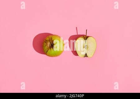 Design alimentaire. Composition de la pomme verte entière et de la moitié de la pomme coupée sur fond de corail rose Banque D'Images