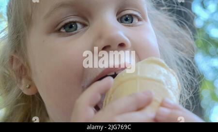 Une petite fille mignonne mange de la glace à l'extérieur. Portrait en gros plan d'une fille blonde assise sur le banc du parc et mangeant de la glace. Odessa Ukraine Banque D'Images