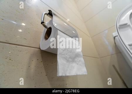 Gros plan d'un rouleau de papier toilette suspendu sur un mur lumineux dans les toilettes, mise au point sélective Banque D'Images